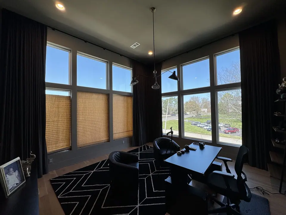 Full-height dark drapery framing corner windows with woven shades on the lower glass