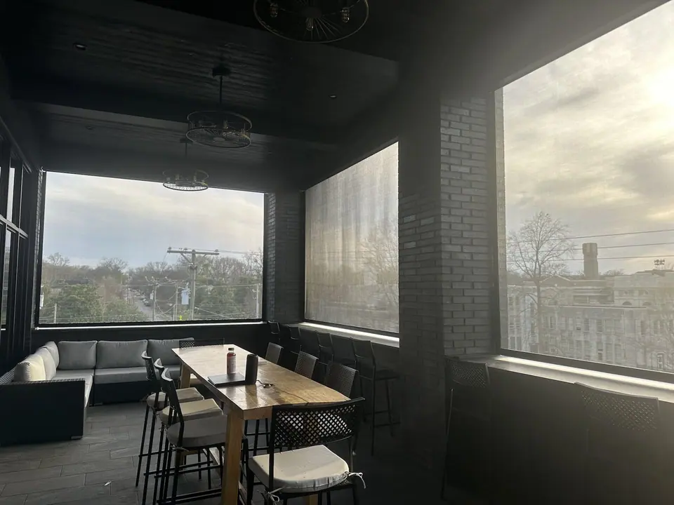 Broad solar shades filtering sunlight around a covered outdoor dining area