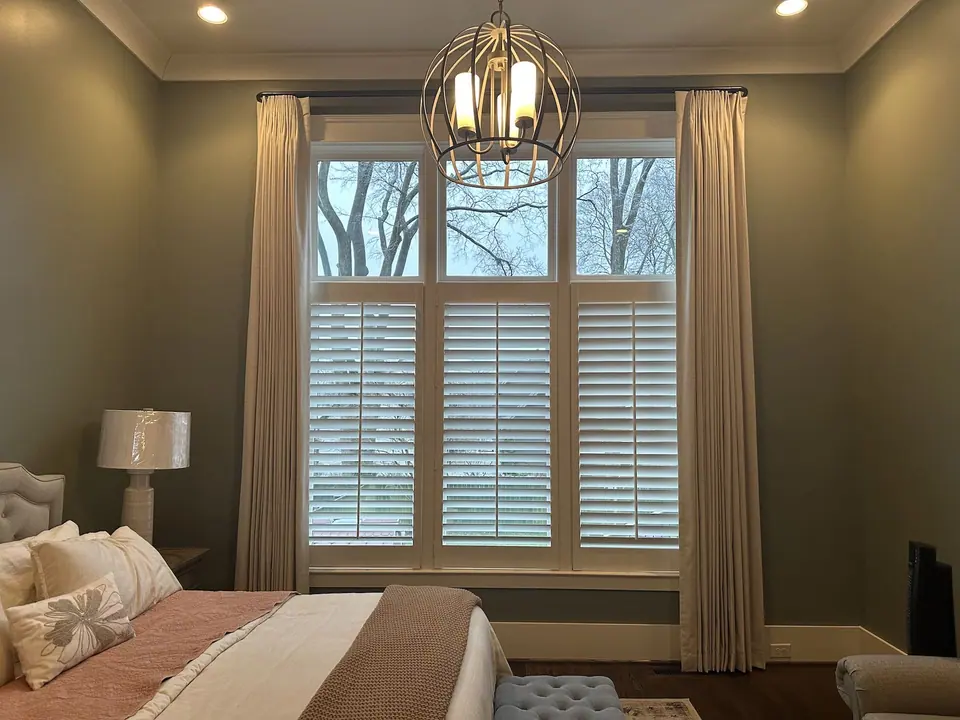 White café-height shutters covering the lower bedroom windows beneath cream drapery